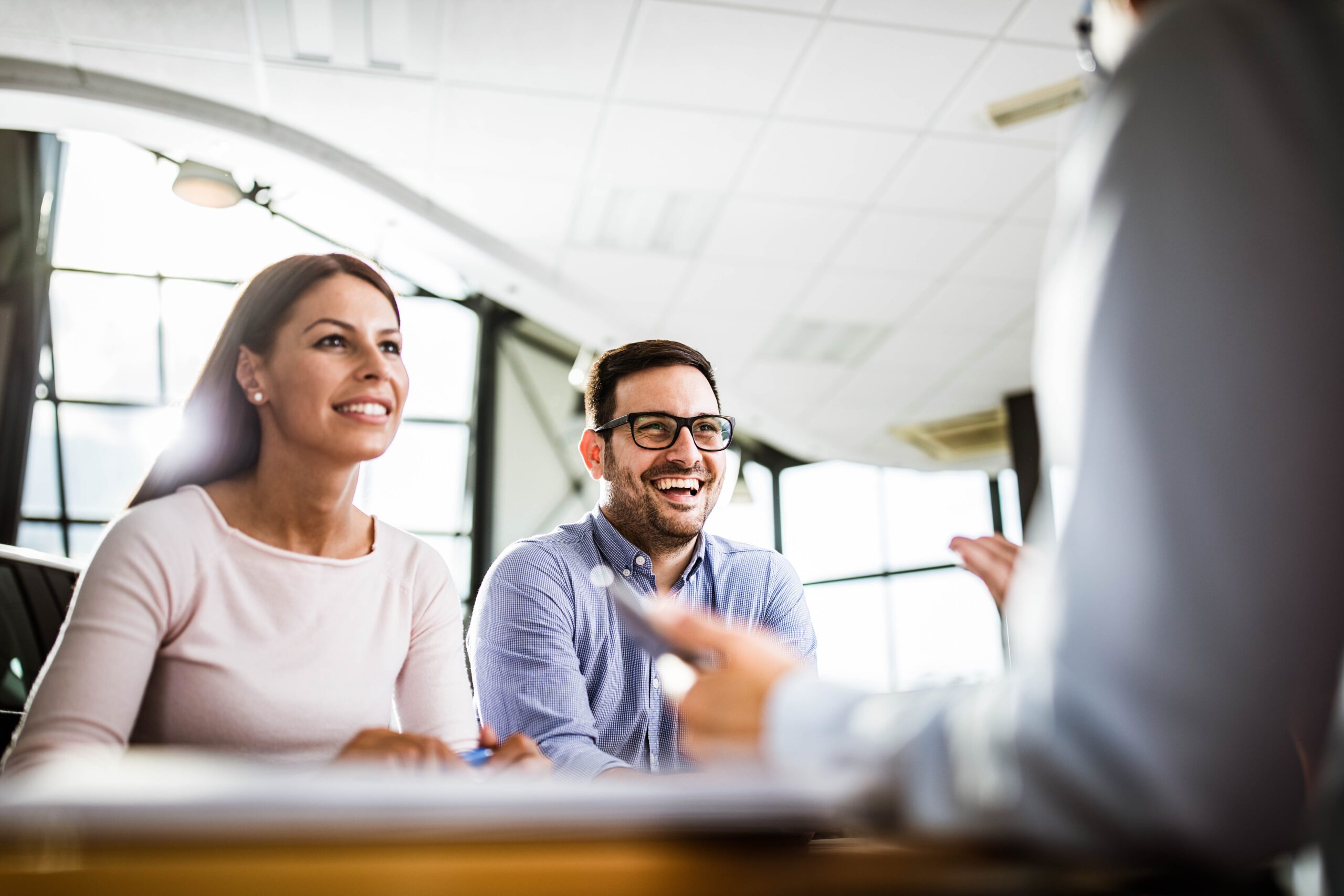 Young happy couple communicating with their financial advisor on a meeting in the office. Focus is on man.