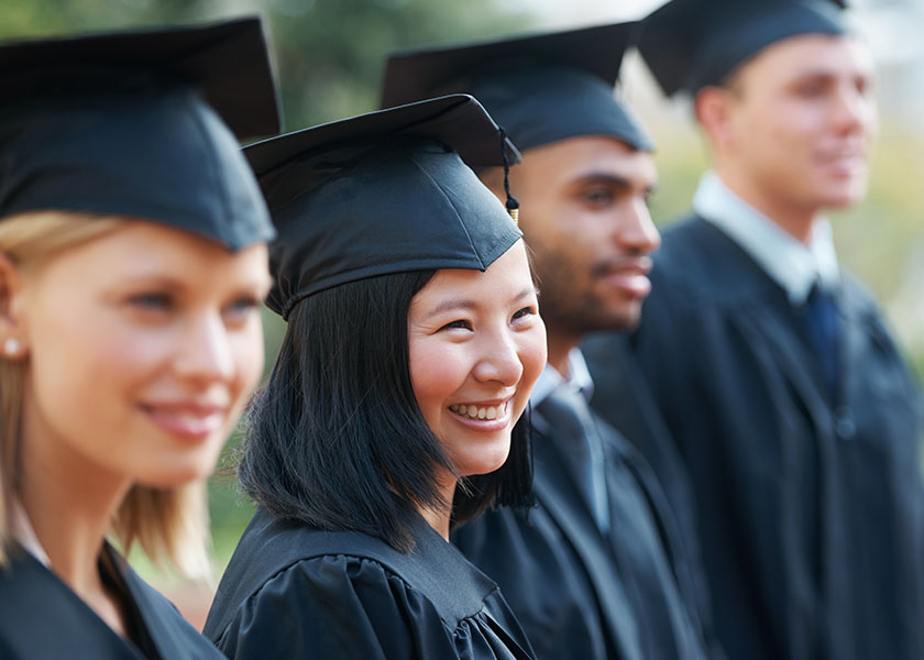 Young college graduates holding their diplomas while standing in a row and smiling